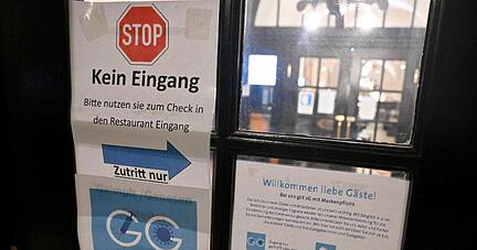Diverse Schilder zum Einhalten der Corona-Schutzmaßnahmen hängen am Eingang zu einer Gaststätte.