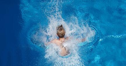 Ein Junge springt in einem Freibad ins Wasser.