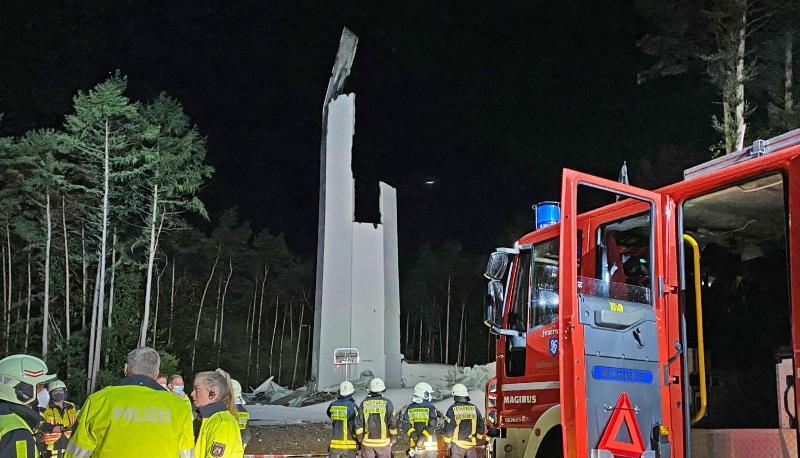 Feuerwehrleute und Polizisten stehen vor den Resten des Turms einer Windenergieanlage. Das fast 240 Meter hohe Windrad ist in sich zusammengestürzt.