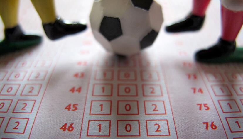 Ein Fußball und vier Spielerbeine auf einem Wettschein für Fußballbegegnungen. Ein Fußball und vier Spielerbeine auf einem Wettschein für Fußballbegegnungen.