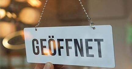 Ein Wendeschild mit der Aufschrift "geöffnet" wird umgedreht. Ein Wendeschild mit der Aufschrift "geöffnet" wird umgedreht.