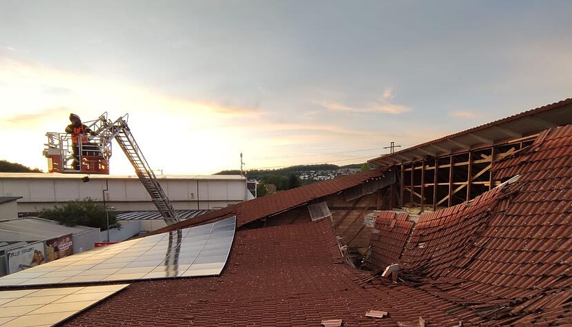 Vom Korb einer Drehleiter heraus kontrolliert ein Feuerwehrmann den eingest&uuml;rzten Dachbereich.