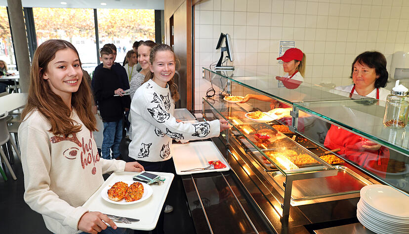 Emilia und Verena, beide 13 Jahre alt, freuen sich auf die leckeren Pizzabrötchen, die es an diesem Tag in der Mensa des Albert-Schweitzer-Gymnasiums gibt. Wie immer zubereitet von Eltern des Kochteam-Vereins.
