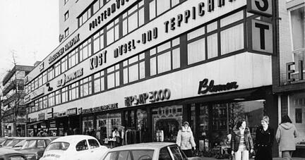 Ansicht des Shoppinghauses an der Allee mit seinem vielfältigen Angebot. Die Parkplätze mit Parkuhren sind heiß begehrt. Undatierte Aufnahme.