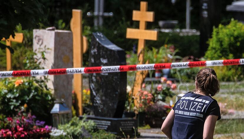 Eine Polizistin geht über den abgesperrten Teil an einem Tatort auf einem Friedhof.