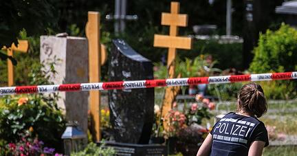 Eine Polizistin geht über den abgesperrten Teil an einem Tatort auf einem Friedhof.