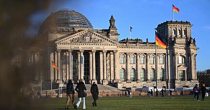 Menschen gehen bei schönem Wetter über die Wiese vor dem Reichstagsgebäude mit dem Bundestag in Berlin.