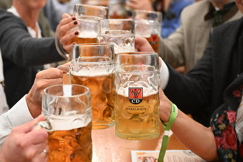 Besucher des Cannstatter Volksfests stoßen bei der Eröffnung mit Bierkrügen an.