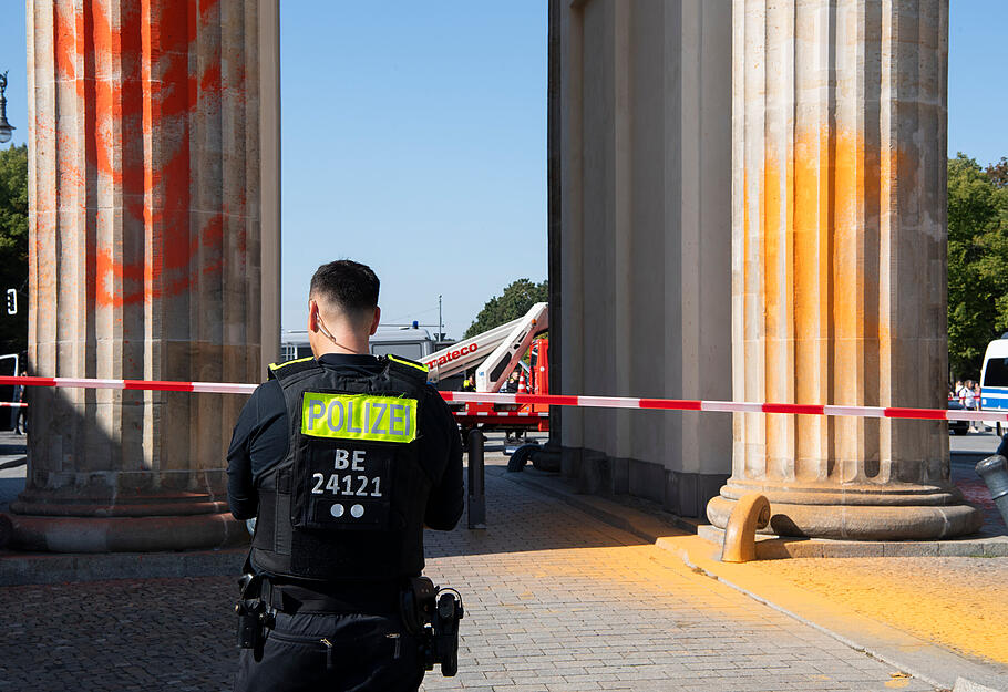 Polizisten stehen am Brandenburger Tor, das Mitglieder der Klimaschutzgruppe Letzte Generation am Sonntagvormittag mit oranger Farbe angespr&uuml;ht haben.