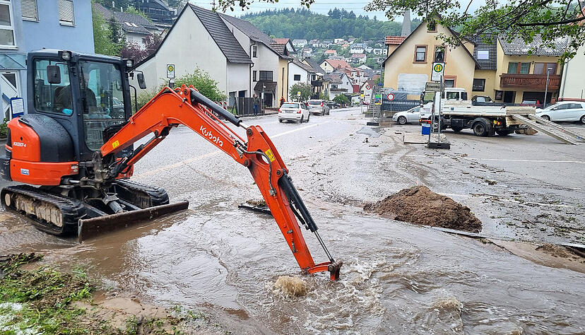 Mit einem kleinen Bagger wird im Stadtteil Altenbach versucht, den Bestbach freizuschaufeln, um das Wasser von der überfluteten Straße abfließen zu lassen.