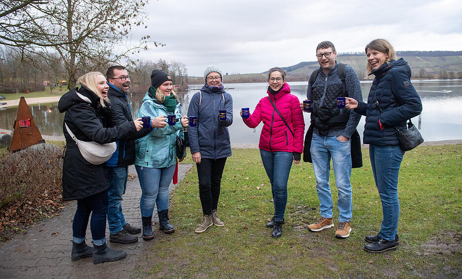 Besucher genießen winterliche Leckereien und heiße Getränke am See.
