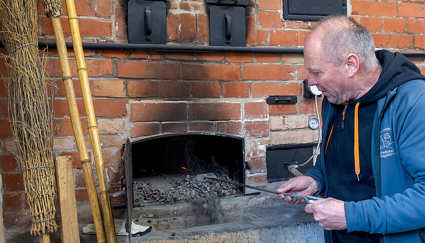 Rolf Laidig schiebt mit der Krücke die Glut aus dem Ofen. Dieser wird danach mit dem Reisigbesen und einem nassen Lappen ausgewischt, damit der Boden sauber ist. Rolf Laidig schiebt mit der Krücke die Glut aus dem Ofen. Dieser wird danach mit dem Reisigbesen und einem nassen Lappen ausgewischt, damit der Boden sauber ist.