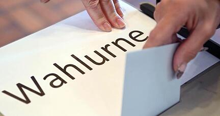 In einem Wahllokal wird ein Stimmzettel in eine Wahlurne geworfen.