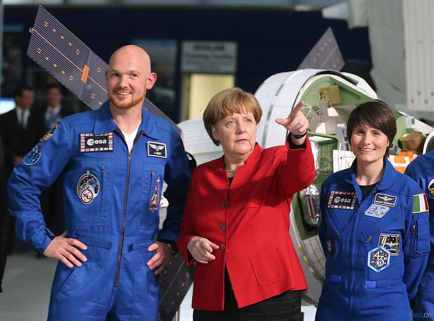 Bundeskanzlerin Angela Merkel (CDU, M), der deutsche Astronaut Alexander Gerst und die italienische Astronautin Samantha Cristoforetti stehen am Mittwoch in Köln beim Besuch im Europäischen Astronautenzentrum (EAC) neben der Raumkapsel Orion. Diese soll in Zukunft Menschen zum Mond, zu Asteroiden und vielleicht sogar zum Mars bringen. Foto: dpa