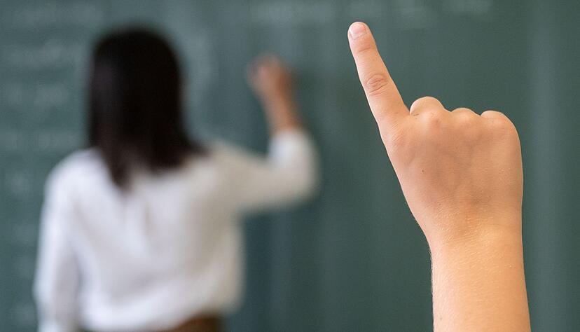 Ein Schüler meldet sich, während die Lehrerin an die Tafel schreibt. Ein Schüler meldet sich, während die Lehrerin an die Tafel schreibt.