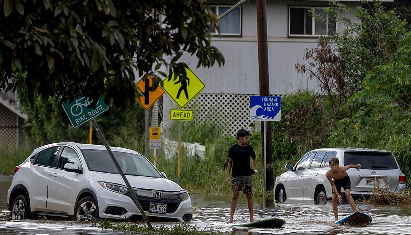 Zwei Jugendliche surfen in Waialua neben einem liegengebliebenen Fahrzeug im Hochwasser.