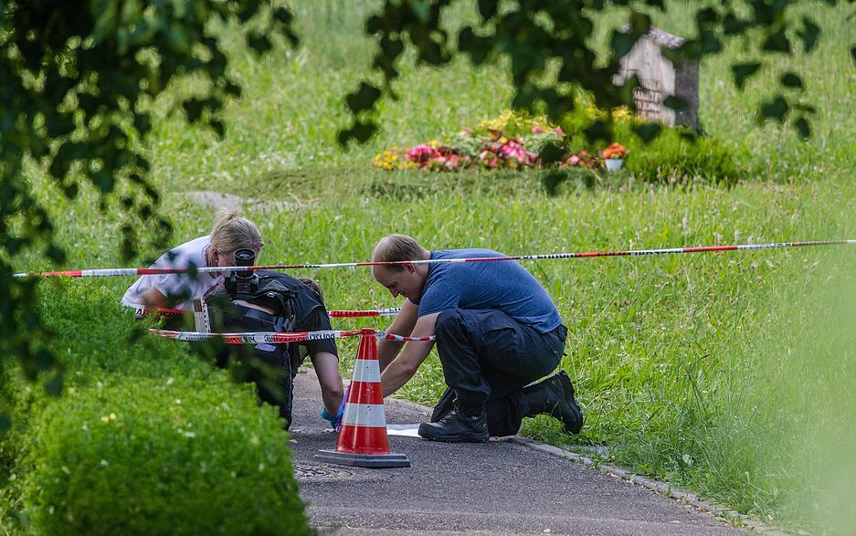Mitarbeiter der Spurensicherung suchen nach Spuren an einem Tatort auf einem Friedhof. Durch den Wurf eines explodierenden Gegenstands auf eine Trauergemeinde gab es mehrere Verletzte. Mitarbeiter der Spurensicherung suchen nach Spuren an einem Tatort auf einem Friedhof. Durch den Wurf eines explodierenden Gegenstands auf eine Trauergemeinde gab es mehrere Verletzte.