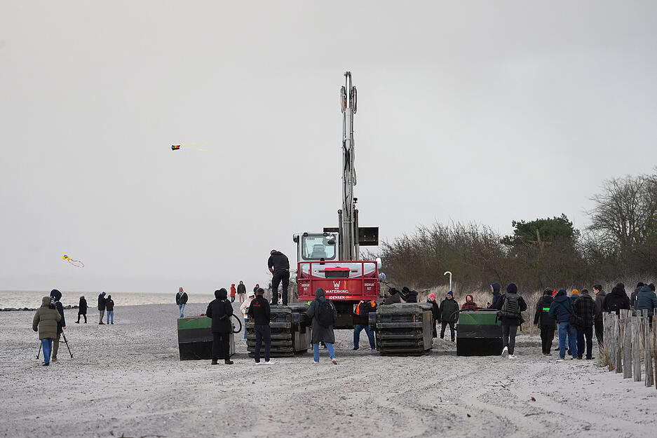Ein Spezial-Schwimmbagger (M) steht zwischen Schwimmpontons am Strand bei Niendorf, wo ein Wal im flachen Wasser gestrandet ist.
