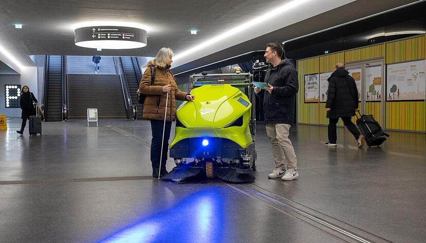 Psychologe Johannes Kraus spricht in der Fu&szlig;g&auml;ngerunterf&uuml;hrung am Hauptbahnhof neben einem Reinigungsroboter mit der sehbehinderten Gertrud Vaas.