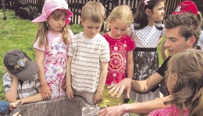 Was macht der denn da? Philipp Thoss zeigt den Mesenokindern wie eine Schieferplatte bearbeitet wird. Der Dachdecker will einen Einblick in seinen Beruf geben. Foto: Bernd Karr