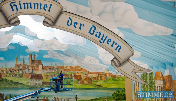 Ein Arbeiter auf einem Kran montiert am 13.08.2013 auf dem Oktoberfestgelände in München (Bayern) Elektoanschlüsse unter die mit langen blauen Stoffbahnen und weissen Wolken abgehangene Dachkonstruktion eines Bierzeltes. Seit dem 15. Juli 2013 wird das größte Volksfest der Welt aufgebaut. Das Oktoberfest dauert dieses Jahr vom 21. September 2013 - 06. Oktober 2013. Foto: Peter Kneffel/dpa +++(c) dpa - Bildfunk+++