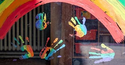 Kinderhände und ein Regenbogen sind an einer Kita zu sehen.