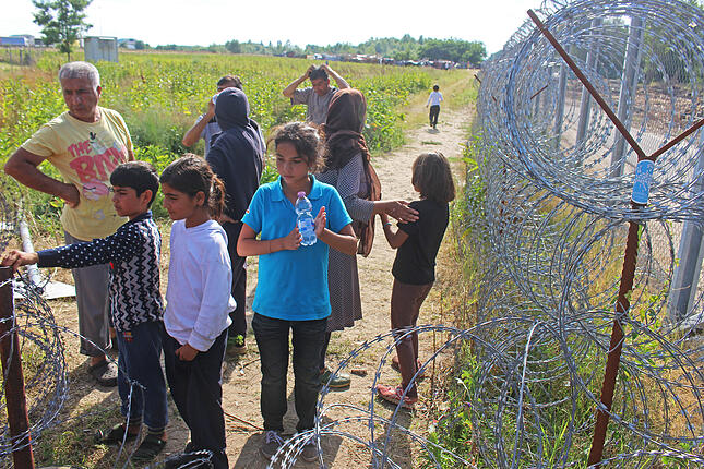 Geflüchtete stehen am 19.07.2016 im Elendslager von Röszke, Ungarn, an der ungarisch-serbischen Grenze am Grenzzaun. Seit mehr als zwei Wochen schiebt Ungarn Asylsuchende über die grüne Grenze nach Serbien zurück. Internationale Organisationen halten das für rechtswidrig. Im ungarisch-serbischen Grenzgebiet stecken um die 1000 Flüchtlinge fest. Foto: Gregor Mayer/dpa (Zu dpa "Ungarn schreckt Flüchtlinge mit harschen Methoden ab" vom 21.07.2016) +++(c) dpa - Bildfunk+++ | Verwendung weltweit