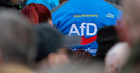 Bei einer Wahlkampfveranstaltung der AfD steht ein Mann mit dem Logo der Partei  in der Menge.