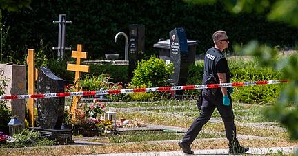 Ein Polizist läuft über den abgesperrten Teil an einem Tatort auf einem Friedhof.