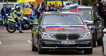 Autos mit Russlandfahnen fahren bei einem Autokorso in Stuttgart unter dem Motto &laquo;Gegen die Diskriminierung russischsprachiger Menschen&raquo; mit. Im Hintergrund ist eine kleine Gegendemonstration mit Pro-Ukrainischen Teilnehmern zu sehen.