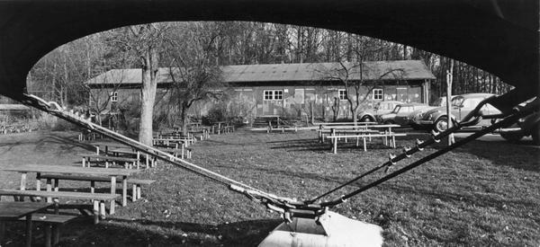 1973. Blick aus dem Zelt auf das Gelände und die Holztische, an denen die Kinder im Sommer ihre Mahlzeiten bekommen.
