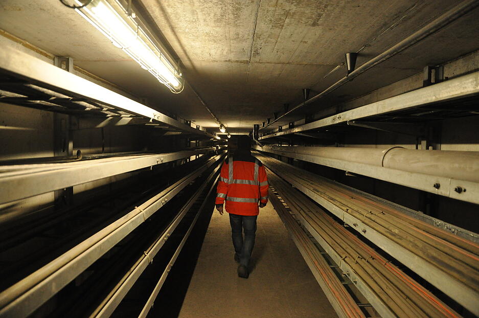 Enge Gänge mit Kabeln an der Seite führen unter den Tunnelröhren zu den Abluftschächten. Bis vor Kurzem war das der einzige Zugang. Jetzt haben Arbeiter zwischen den Tunnelröhren einen großzügigen Zugang mit Treppenhaus und Lastenaufzug in den Untergrund betoniert. Er dient während der anstehenden fünfjährigen Bauphase als Hauptzugang für die Baustellenlogistik. Enge Gänge mit Kabeln an der Seite führen unter den Tunnelröhren zu den Abluftschächten. Bis vor Kurzem war das der einzige Zugang. Jetzt haben Arbeiter zwischen den Tunnelröhren einen großzügigen Zugang mit Treppenhaus und Lastenaufzug in den Untergrund betoniert. Er dient während der anstehenden fünfjährigen Bauphase als Hauptzugang für die Baustellenlogistik.