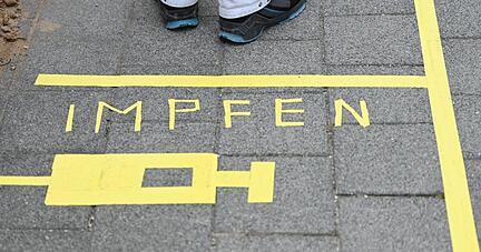 Ein Mann steht an einem Covid-19-Impfcenter hinter der Bodenaufschrift "Impfen".