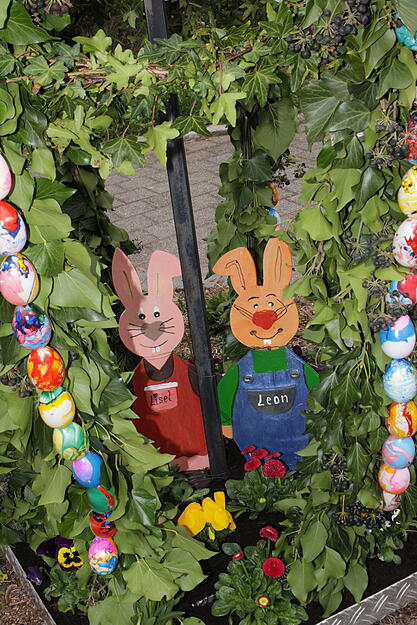 Sie schneiden, b&uuml;ndeln und binden Efeuranken an das gro&szlig;e eierf&ouml;rmige Metallger&uuml;st. Das schm&uuml;cken die Frauen anschlie&szlig;end mit Girlanden aus bunten Kunststoffeiern. Dann platzieren sie im Sockel ein Osterhasenpaar aus Holz und pflanzen in die Sockelwane bunten Fr&uuml;hlingsbl&uuml;mchen.