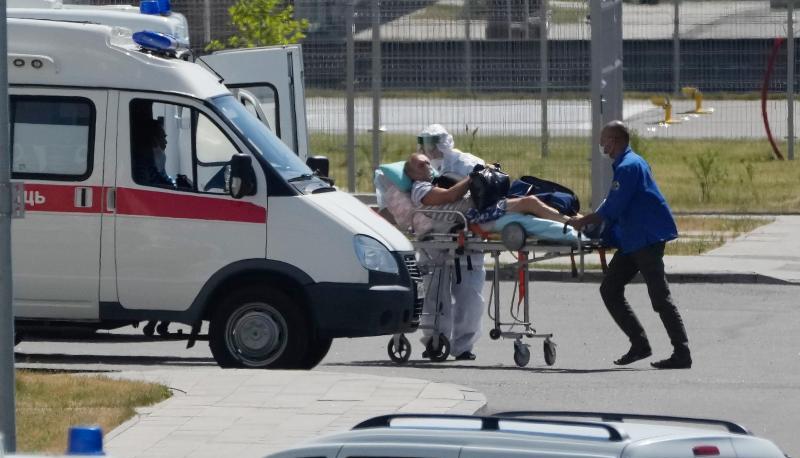 Medizinische Mitarbeiter - einer mit einer speziellen Schutzausrüstung - begleiten einen Mann mit Verdacht auf Covid-19 zu einem Krankenhaus in Kommunarka bei Moskau.