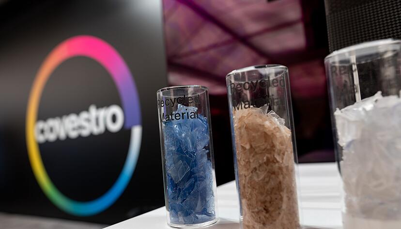 Eine deutsche Firma wird arabisch: Das Logo des Spezialchemie-Konzerns in einem Firmen-Showroom, davor Gläser mit Covestro-Materialien.