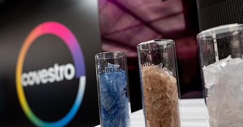 Eine deutsche Firma wird arabisch: Das Logo des Spezialchemie-Konzerns in einem Firmen-Showroom, davor Gläser mit Covestro-Materialien.