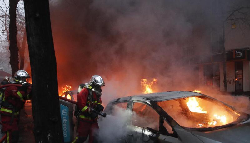Feuerwehrleute löschen während eines Protestes auf einer Straße ein brennendes Auto.