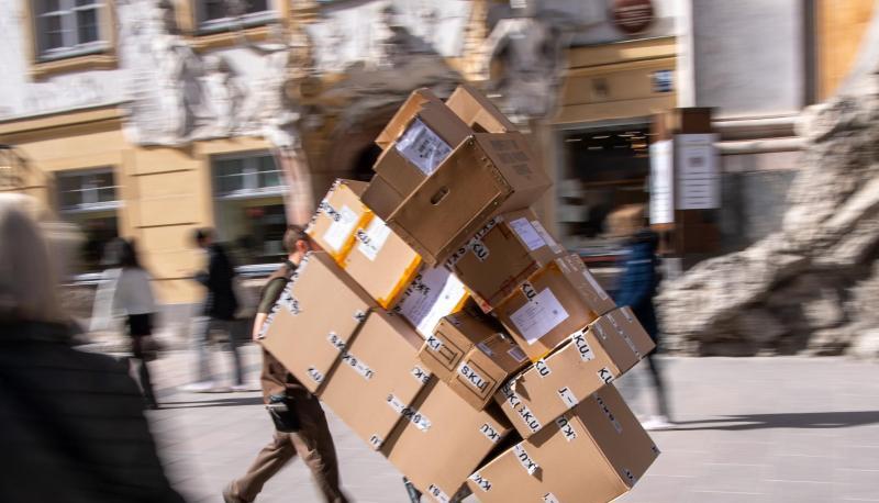 Ein Paketzulieferer transportiert mit einer Sackkarre mehrere Pakete durch die Fußgängerzone.