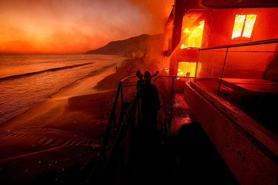 Feuerwehrleute arbeiten von einer Terrasse aus, während das Palisades-Feuer in Malibu, Kalifornien, ein Grundstück am Strand verbrennt. Feuerwehrleute arbeiten von einer Terrasse aus, während das Palisades-Feuer in Malibu, Kalifornien, ein Grundstück am Strand verbrennt.