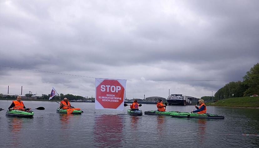 Klimaaktivisten der «Letzten Generation» in Warnwesten blockieren mit Kajaks die Kanalzufahrt zum Ölhafen. Zudem haben sie ein Absperrband mit einem Stoppschild über den Kanal gespannt. Es hat die Aufschrift: «Stop - wegen Klimakatastrophe geschlossen». Klimaaktivisten der «Letzten Generation» in Warnwesten blockieren mit Kajaks die Kanalzufahrt zum Ölhafen. Zudem haben sie ein Absperrband mit einem Stoppschild über den Kanal gespannt. Es hat die Aufschrift: «Stop - wegen Klimakatastrophe geschlossen».