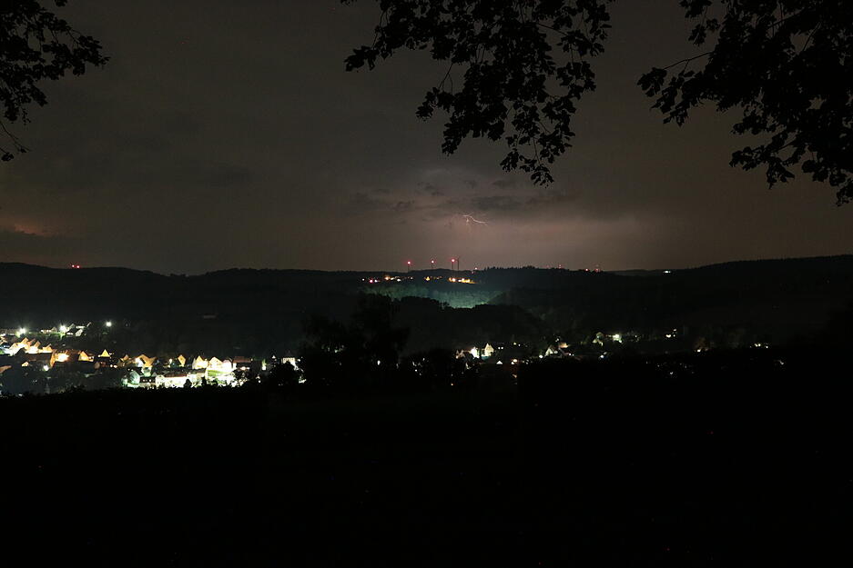 Wetterleuchten über der Burg Aschhausen, innerhalb der 15 Sekunden Belichtungszeit ist ein Blitz im Himmel erschienen. Im Tal nach Bieringen beleuchten Autoscheinwerfer den Wald.