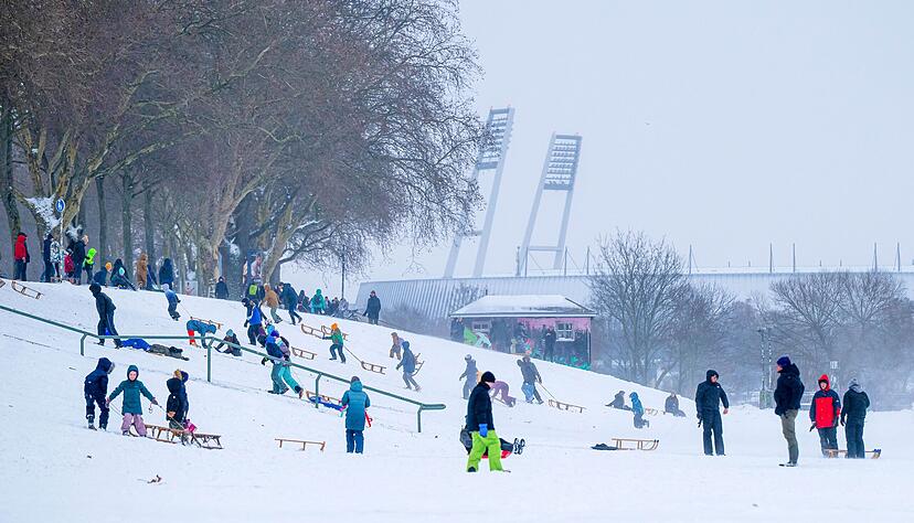 Zahlreiche Menschen nutzen den verschneiten Osterdeich in Bremen zum Schlitten-, Ski oder Snowboardfahren. Unterdessen wurde die Bundesliga-Partie im Weserstadion (Bildhintergrund) abgesagt.