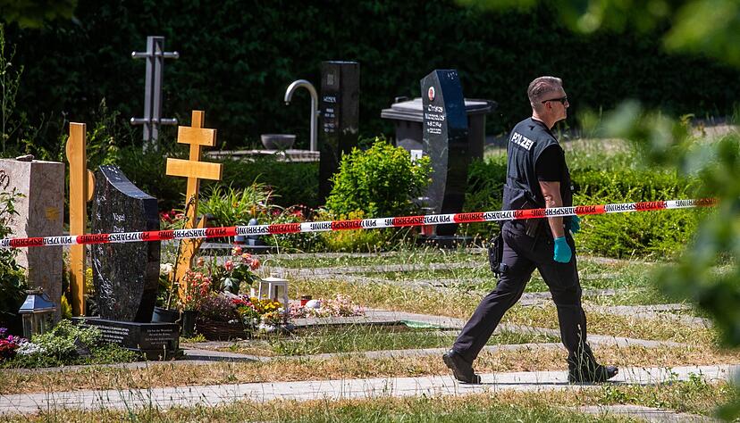 Ein Polizist geht über den abgesperrten Teil an einem Tatort auf einem Friedhof in Altbach.
