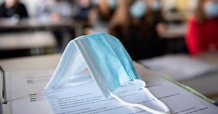 Eine Maske liegt im Unterricht auf Unterlagen.