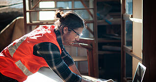 Young and handsome caucasian carpenter in the carpentry shop is working and checking blueprint in laptop to repair a furniture. Young and handsome caucasian carpenter in the carpentry shop is working and checking blueprint in laptop to repair a furniture.