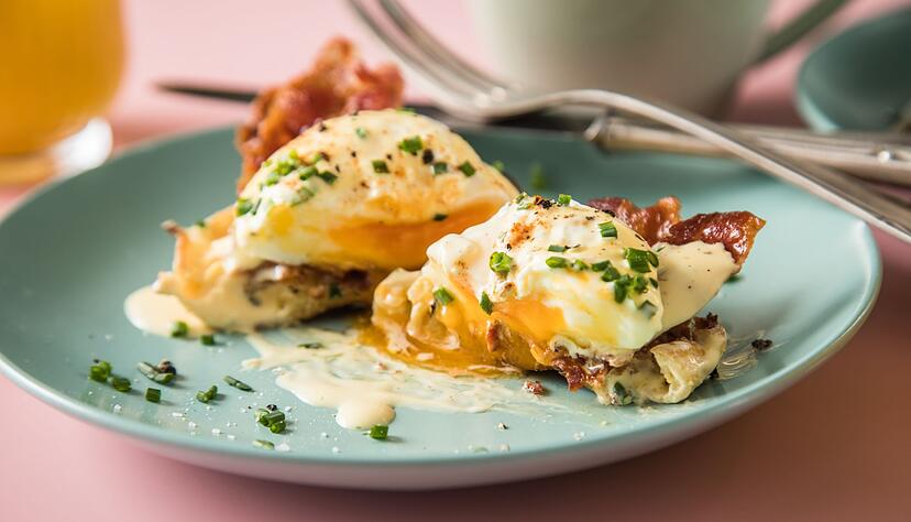 Eggs Benedict aus pochierten Eiern, Sauce Hollandaise, Schnittlauch, Paprika-Pulver, Bacon und halbierten englischen Muffins.