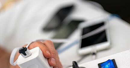 Ein Mann zieht den Stecker eines Ladeger&auml;ts f&uuml;r ein Smartphone aus einer Steckdosenleiste.