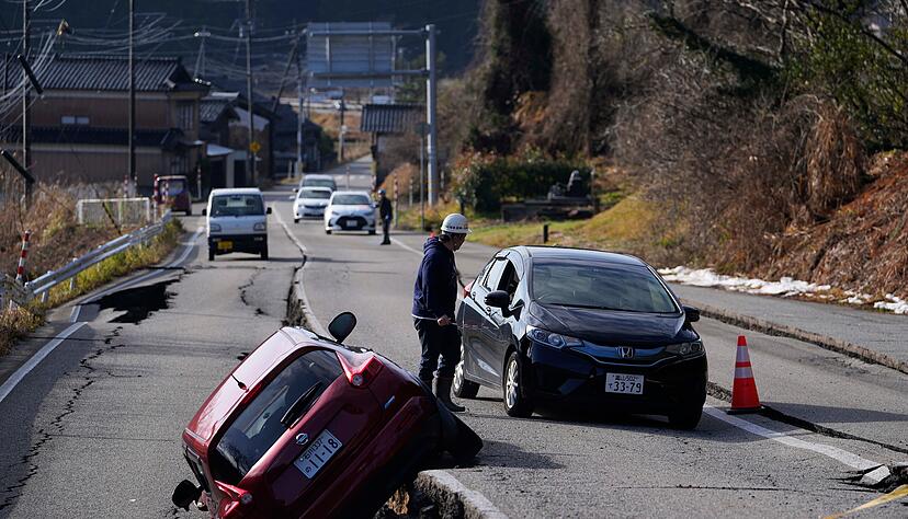 Ein Mann dirigiert einen Autofahrer durch eine beschädigte Straße in der Nähe der Stadt Anamizu auf der Halbinsel Noto am Japanischen Meer, nach einem Erdbeben am 1. Januar 2024.