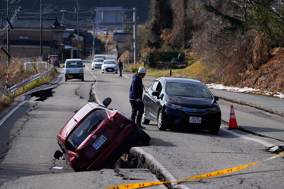 Ein Mann dirigiert einen Autofahrer durch eine beschädigte Straße in der Nähe der Stadt Anamizu auf der Halbinsel Noto am Japanischen Meer, nach einem Erdbeben am 1. Januar 2024.